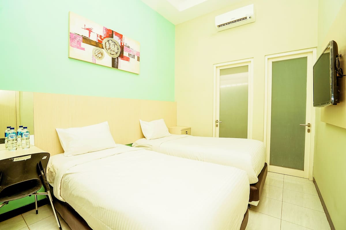 Ein Hotelzimmer mit zwei Betten, einem Schreibtisch mit Stuhl, einem Flachbildfernseher und einem Bild an der Wand.