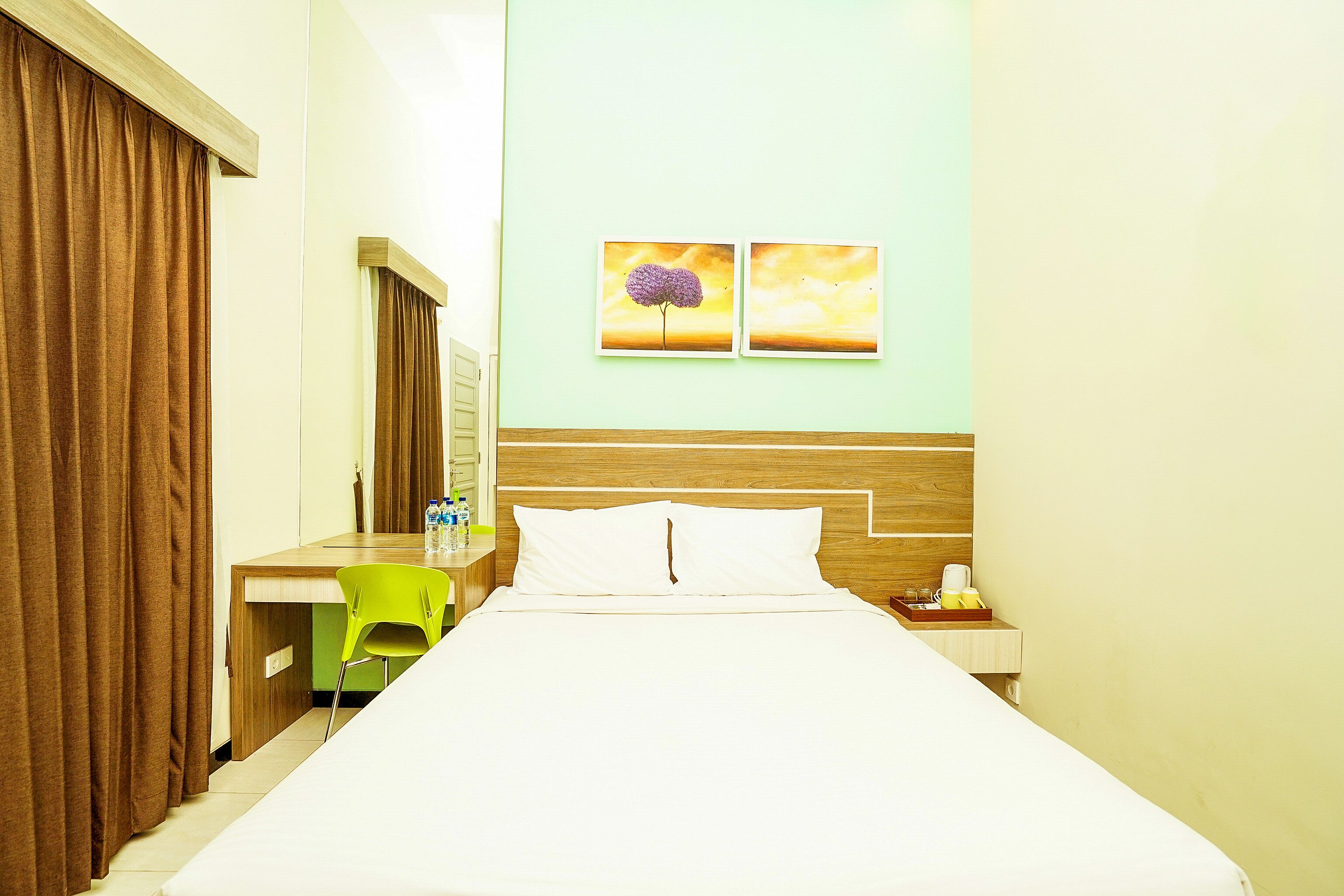 Una habitación de hotel con una cama, un escritorio, una silla y dos cuadros en la pared.