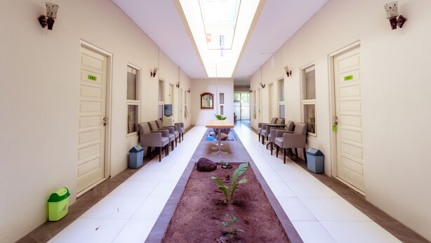 A hotel corridor with a central planter, seating areas, and doors on both sides. - Ardhya Guesthouse Syariah by Ecommerceloka (Sidoarjo)