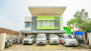A modern two-story building with a flat roof and a green accent wall. In front, there are four cars parked in a row. - Ardhya Guesthouse Syariah by Ecommerceloka (Sidoarjo)