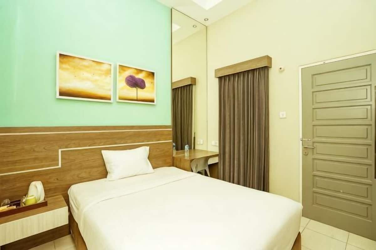 Ein Hotelzimmer mit einem Bett, einem Nachttisch, einem Spiegel, einer Tür und zwei an der Wand befestigten Bildern.
