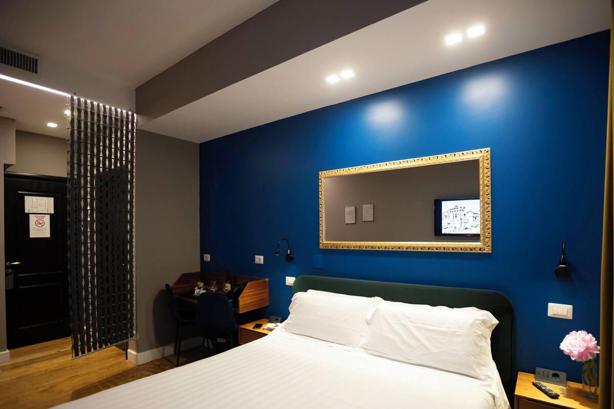 A hotel room with a bed, a desk, a chair, a TV, and a mirror.