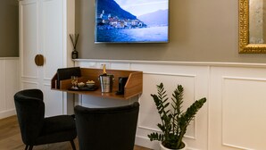 Un salon moderne avec une table basse en bois, deux chaises noires, une plante en pot, un téléviseur à écran plat fixé au mur et un meuble blanc.