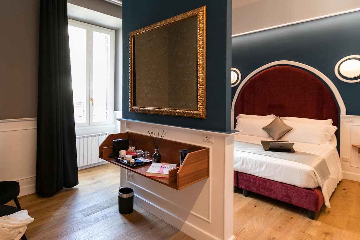A bedroom with a wooden dresser, a mirror, a bed with a red headboard, and a window with curtains.