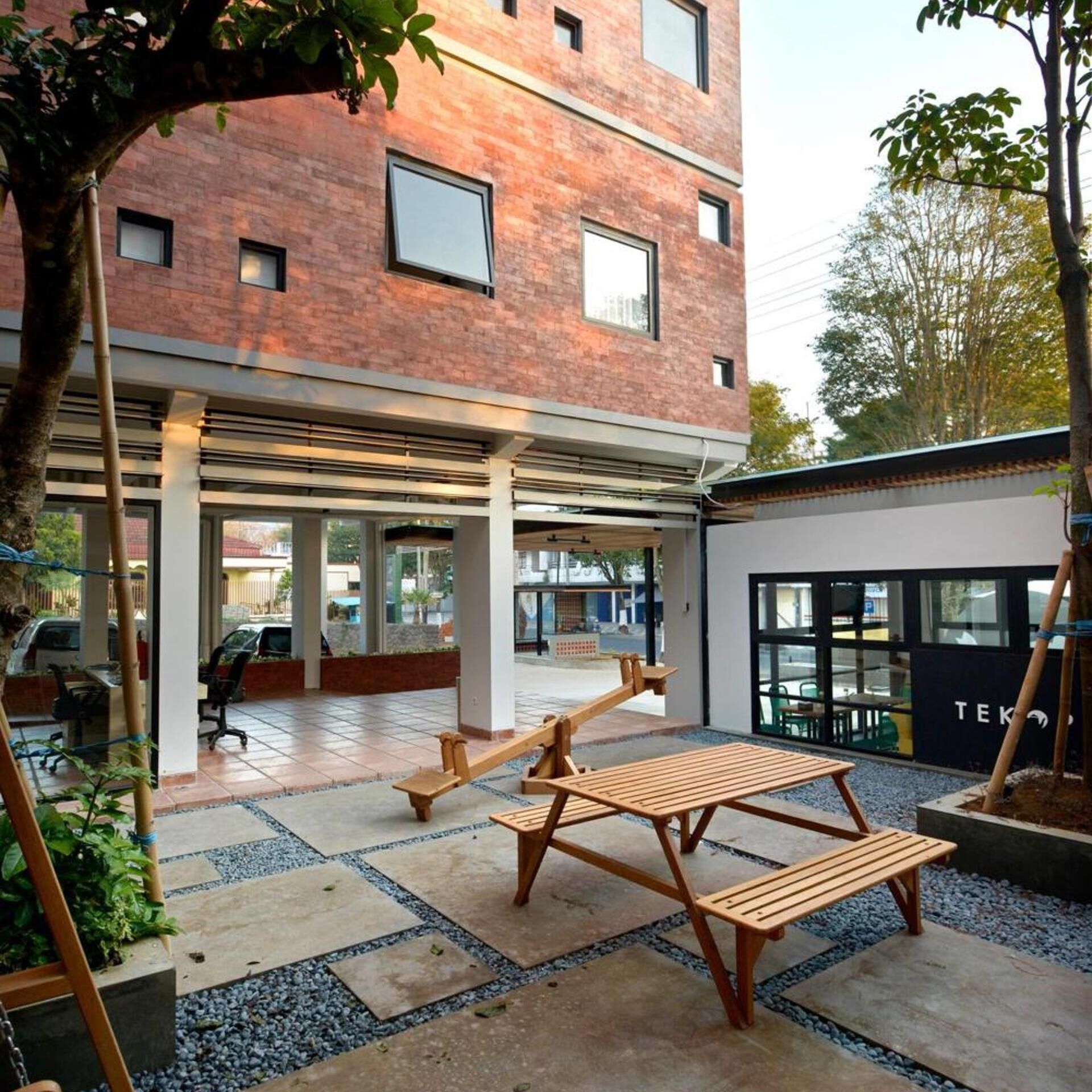 A courtyard with a wooden bench, a tree, and a building with large windows.