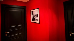 Un pasillo con paredes rojas, una fotografía blanco y negro enmarcada y puertas de madera oscura.