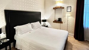 Una habitación de hotel con una cama grande, una mesita de noche, una lámpara y un espejo.