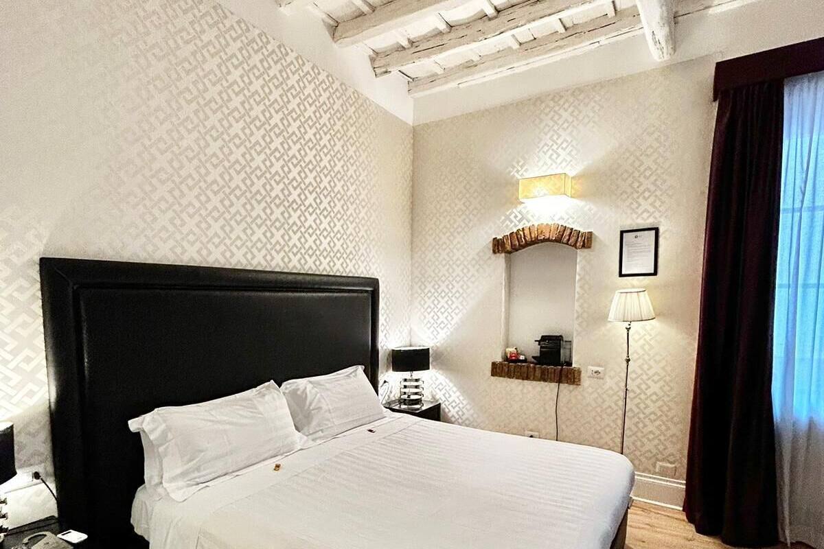 A hotel room with a large bed, a nightstand, a lamp, and a mirror.