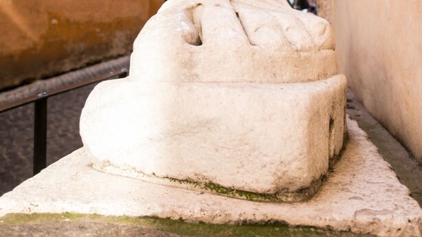 Una escultura de piedra en un entorno urbano, con edificios al fondo.