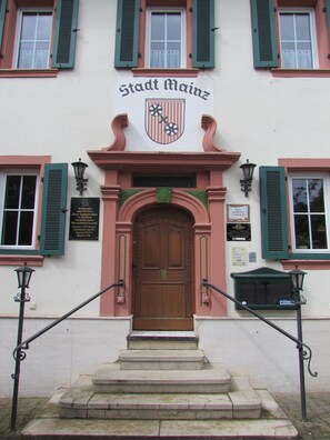 A building with a sign reading "Stadt Mainz" above a wooden door, flanked by two windows with green shutters. - Hotel Stadt Mainz (Schwabenheim an der Selz)