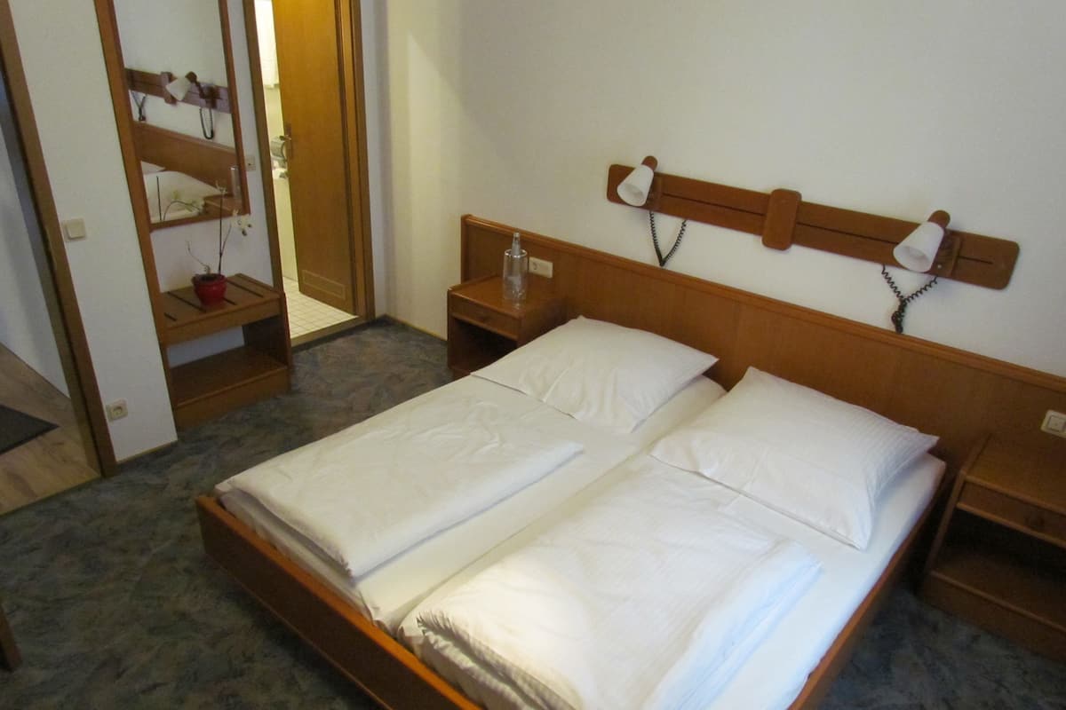Un lit double avec du linge de lit blanc, une tête de lit en bois, des tables de chevet avec des lampes et un miroir au mur.