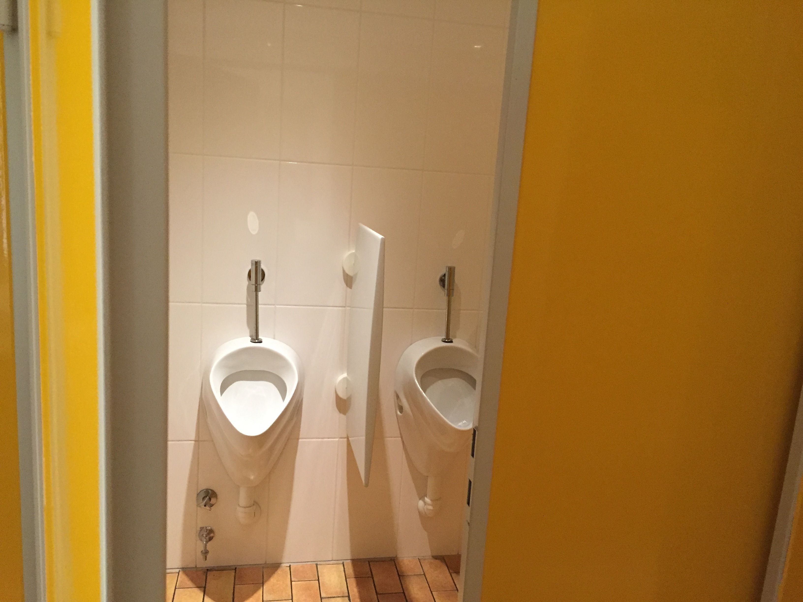 Des toilettes avec deux urinoirs, le tout adossé à un mur recouvert de carreaux blancs.
