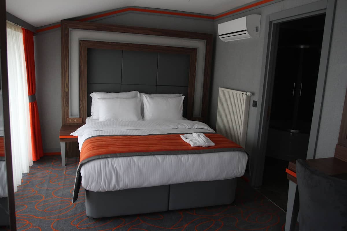 A hotel room with a large bed, a wooden headboard, a desk, and an air conditioning unit.