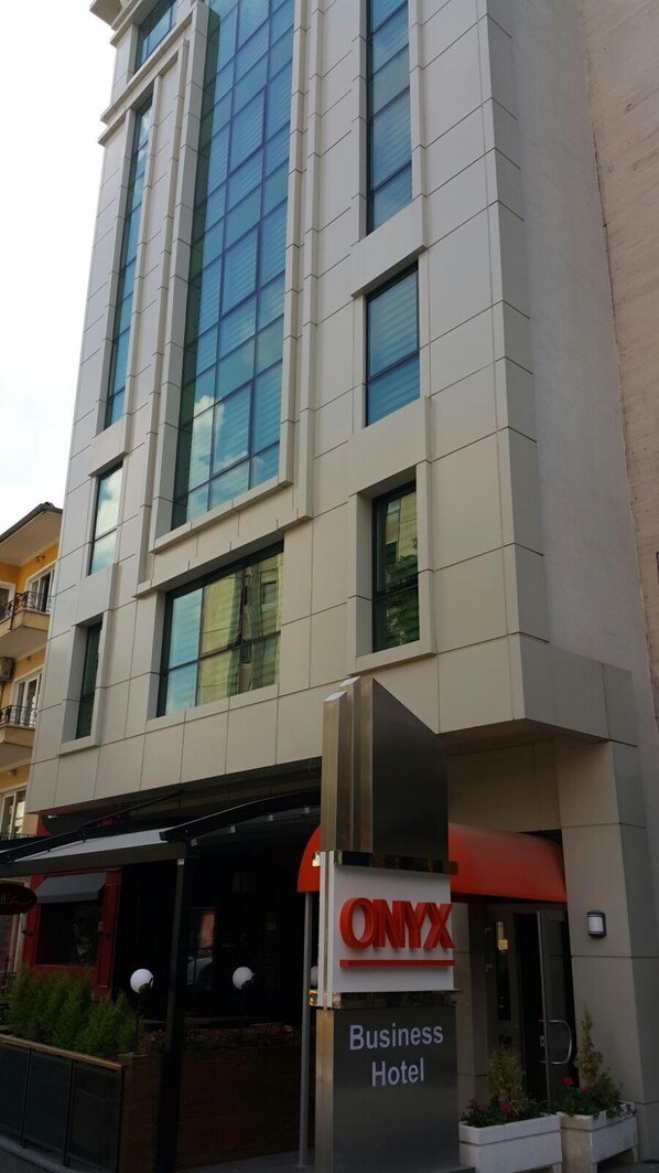 A business hotel with a modern facade, large windows, and a prominent red and white sign.