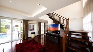 A spacious living room with a large flat-screen TV, a red rug, and a wooden staircase. - PARADISE Pool Villa Pattaya in Tropicana Village (Pattaya)