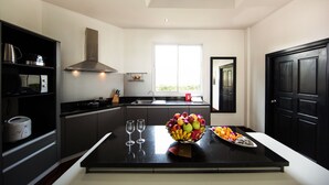 A modern kitchen with a central island, black cabinetry, a stainless steel range hood, and a window providing natural light. - PARADISE Pool Villa Pattaya in Tropicana Village (Pattaya)