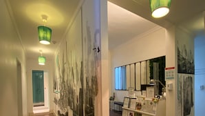 A hallway with a glass partition displaying artwork, a reception desk with framed certificates, and a door at the end. - Green Heart Hostel (Lisbon)