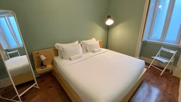 A neatly made bed in a room with green walls, a wooden floor, and a bedside lamp.