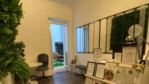 A reception area with a desk, chairs, a display of informational posters, and a view of the outdoor area through a glass door. - Green Heart Hostel (Lisbon)