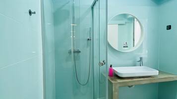 Un baño con ducha de vidrio, lavamanos blanco y espejo redondo.