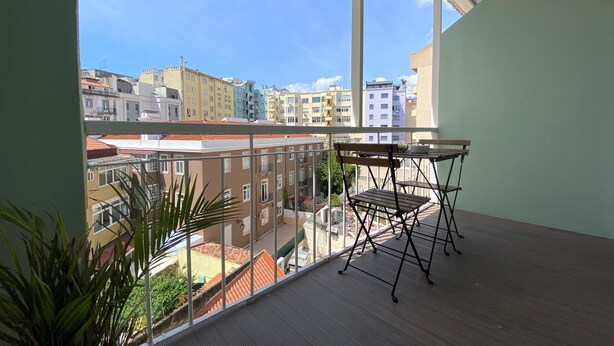 A balcony with a table and chairs, overlooking a cityscape with various buildings. - Green Heart Hostel (Lisbon)