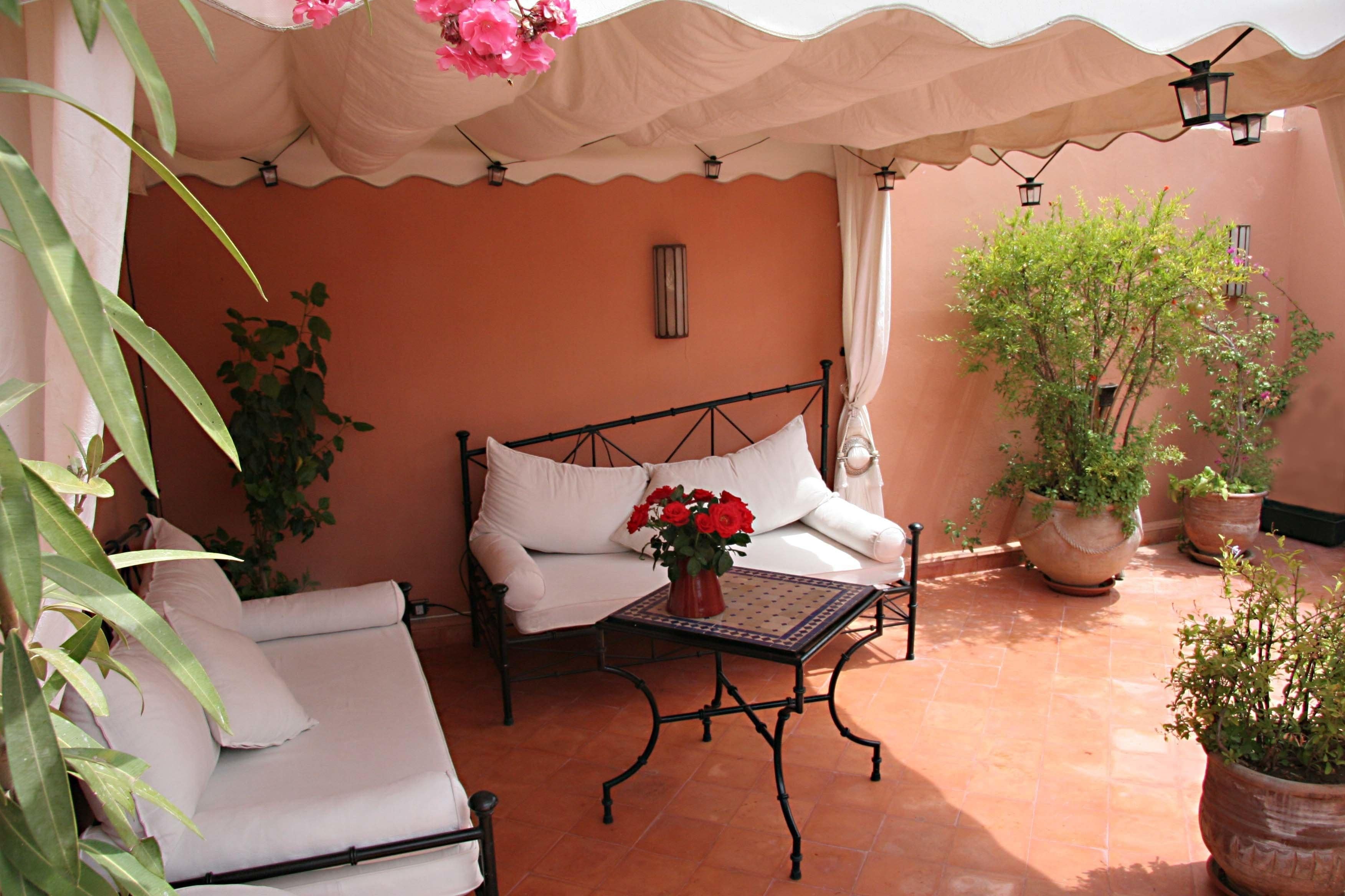 A cozy outdoor seating area with a white sofa, a small table with a vase of flowers, and potted plants.