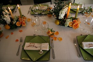 Una mesa dispuesta para una comida, con velas, flores y platos verdes.