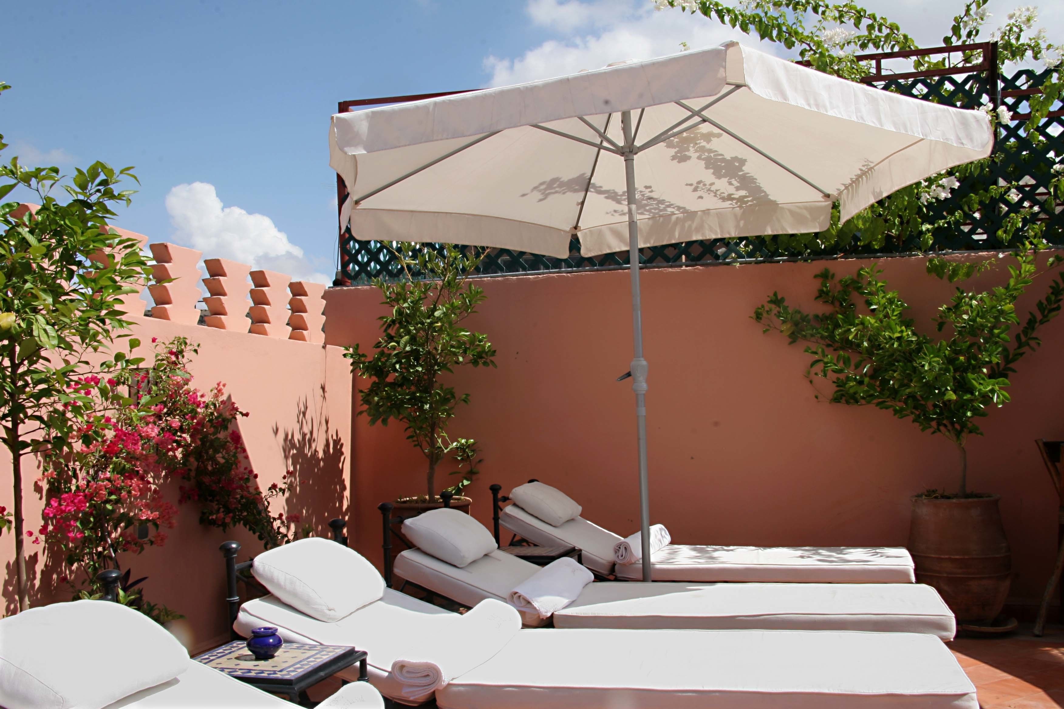 A rooftop terrace with sun loungers, a large umbrella, and potted plants.