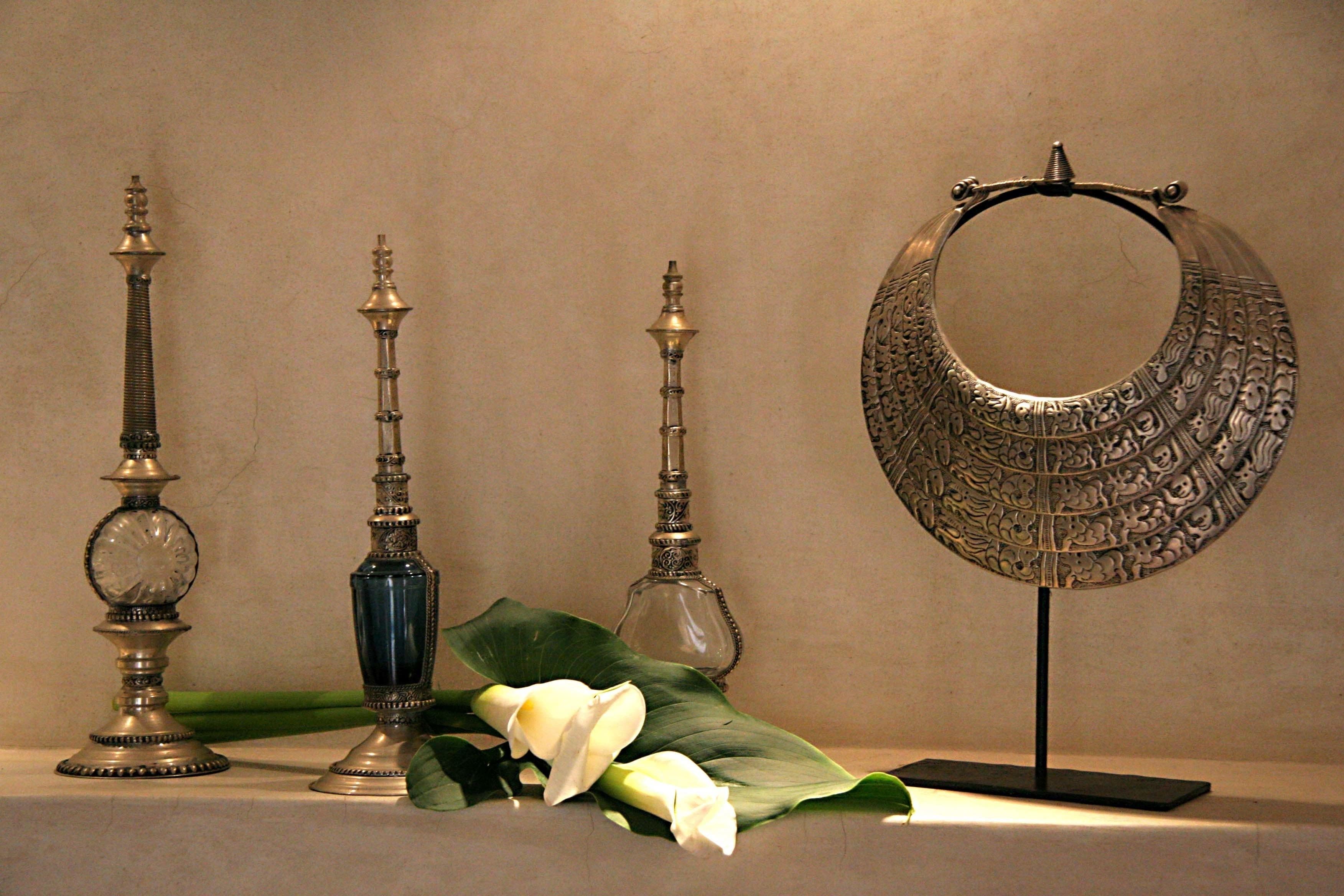 Une exposition d’objets en métal décoratifs, dont un miroir et des chandeliers, agrémentée de fleurs blanches.