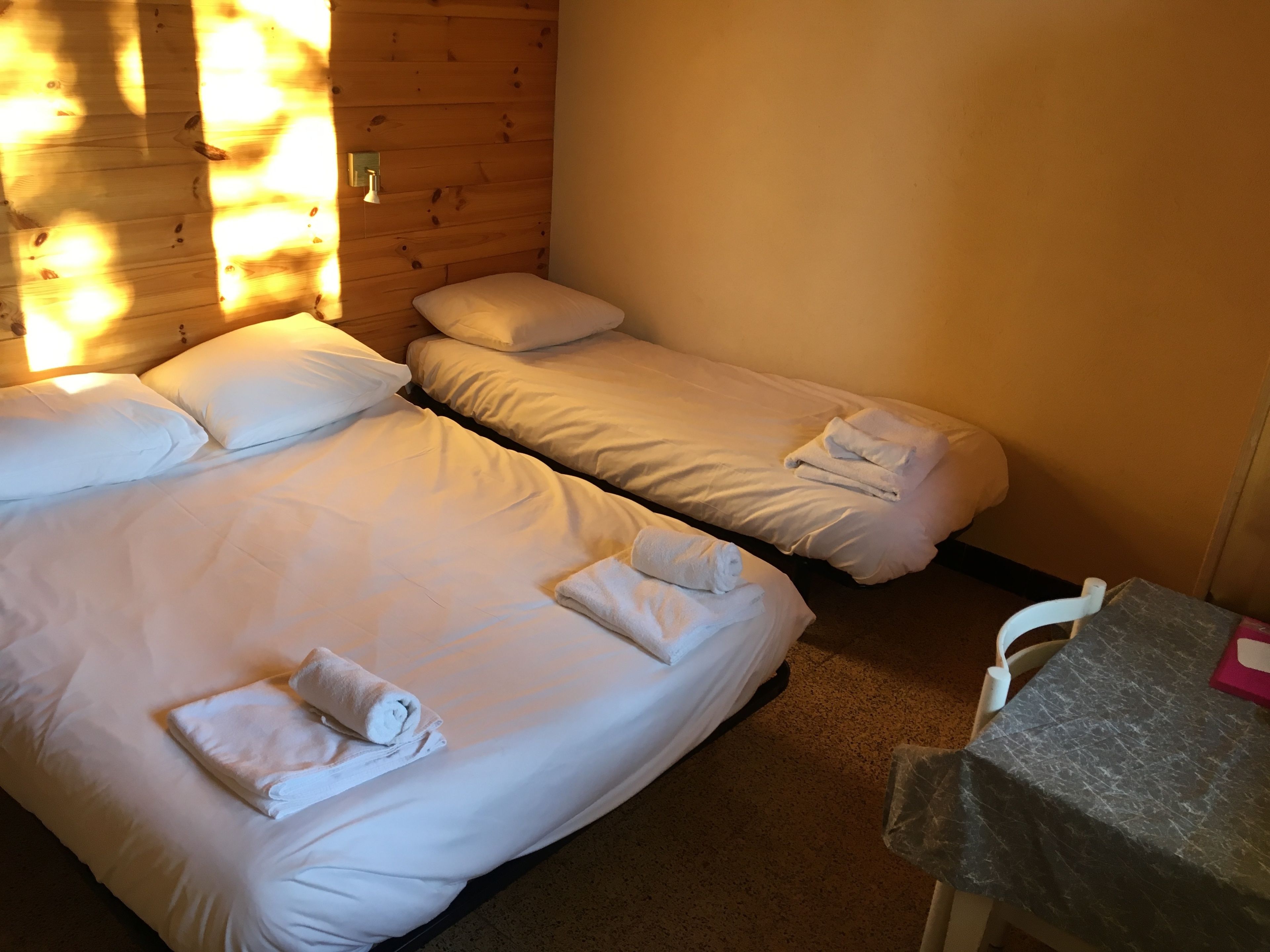 A room with two beds, each with white linens and pillows, and a small table with a tablecloth.