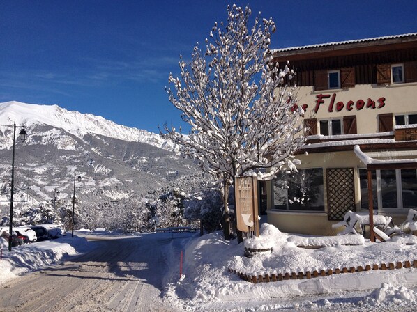 A building with a sign reading "Flocons" and a ski slope in the background. - Hôtel Les Flocons (Enchastrayes)