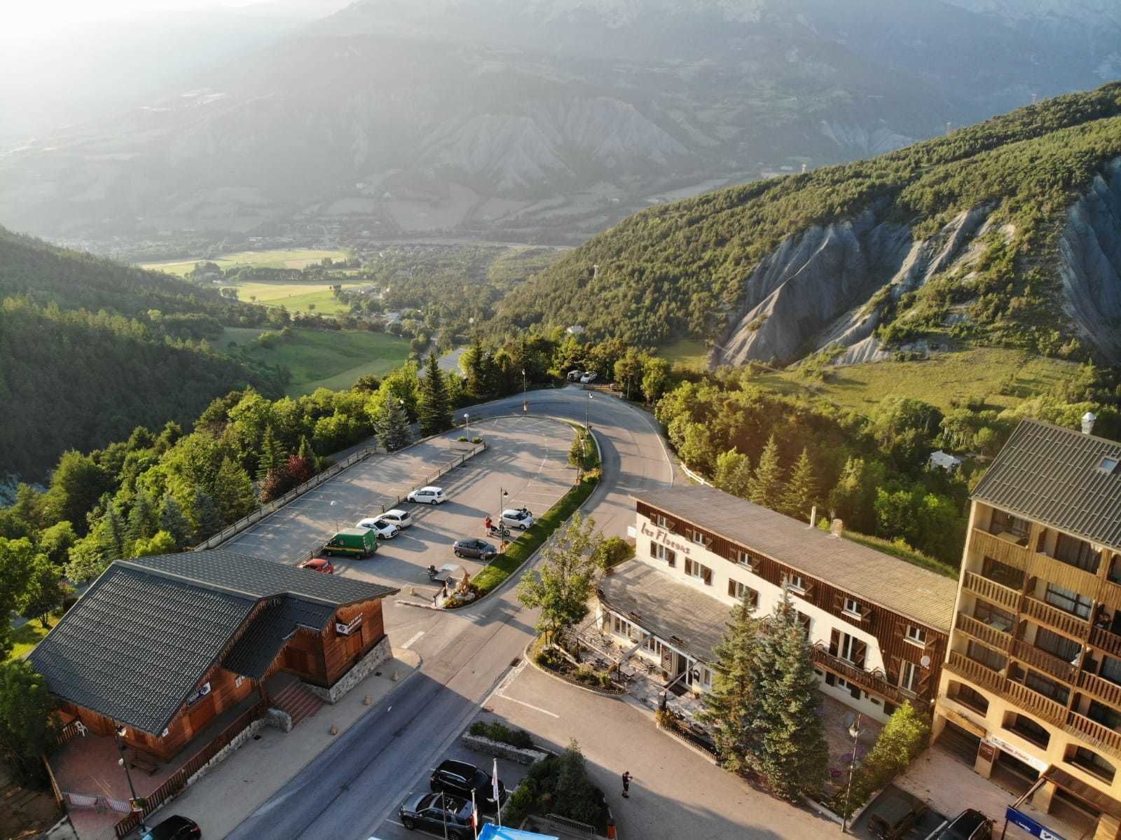 A hotel with a parking lot, a building with a sloped roof, and a mountainous backdrop.