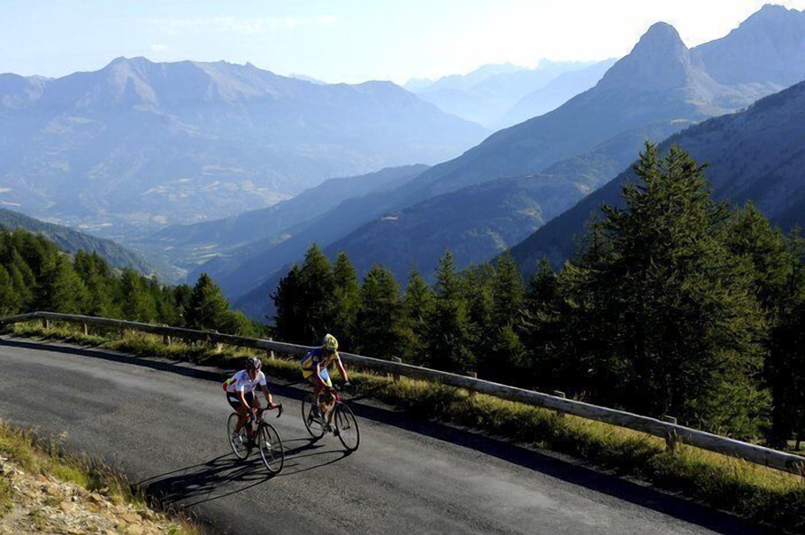 Two cyclists on a paved road with a mountainous backdrop.
