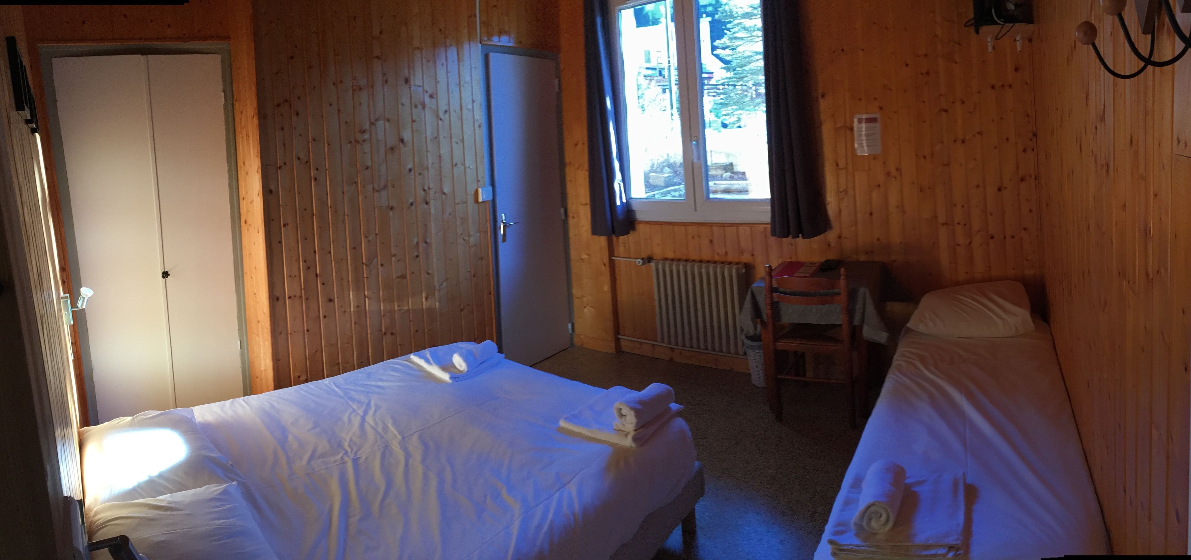 Een kamer met twee bedden, een houten garderobe, een radiator en een raam met gordijnen.
