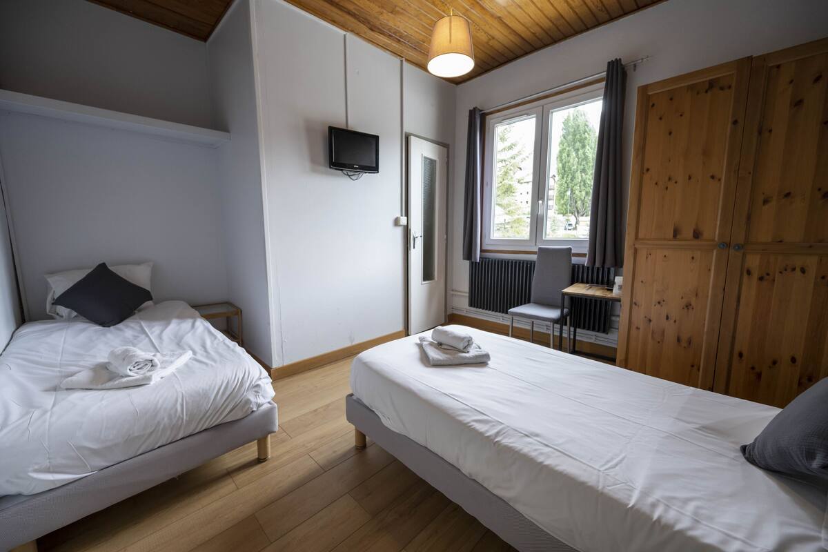 A bedroom with two beds, a TV, a window with curtains, and wooden furniture.