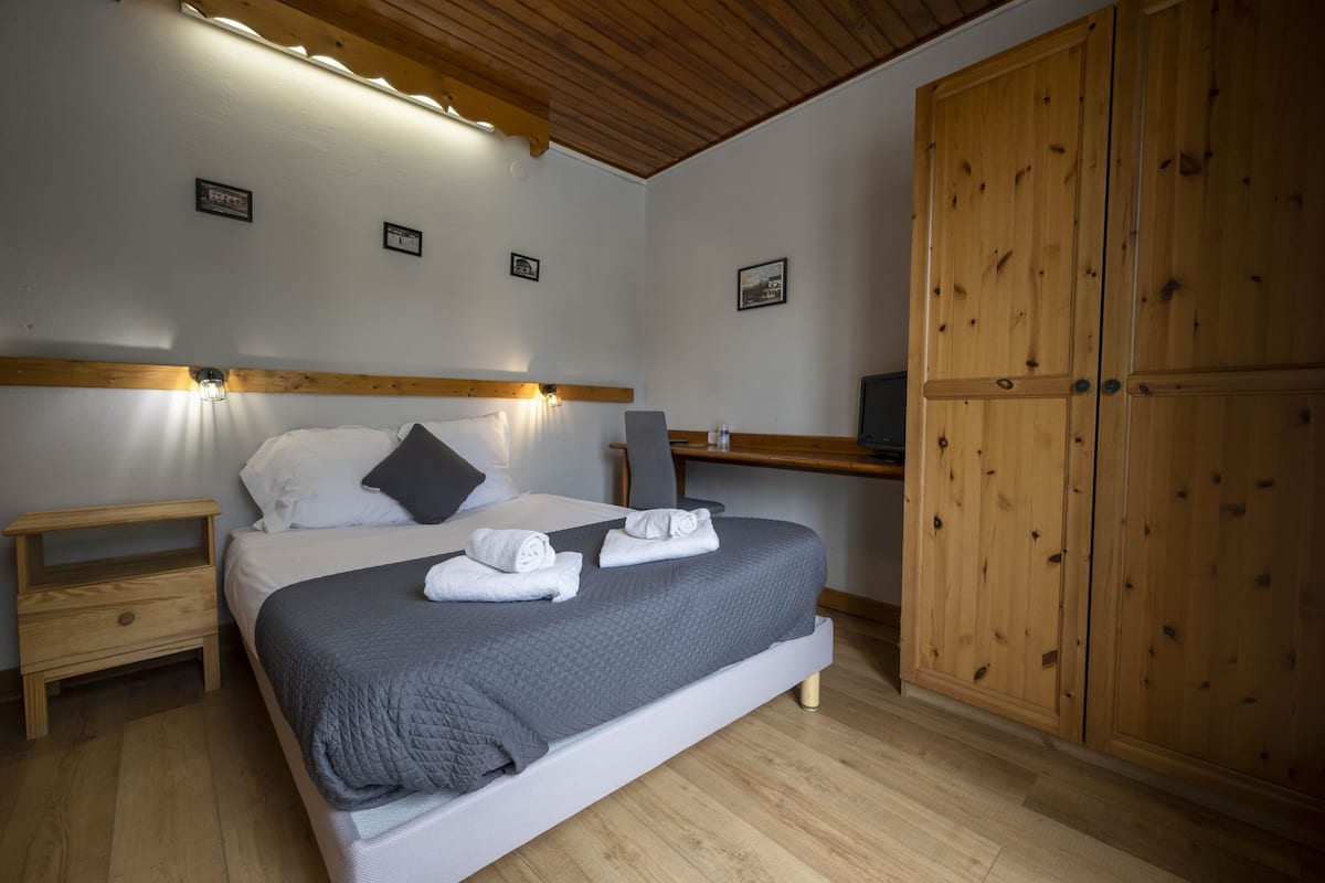A neatly made bed with pillows and towels, a wooden wardrobe, and a bedside table with a lamp.