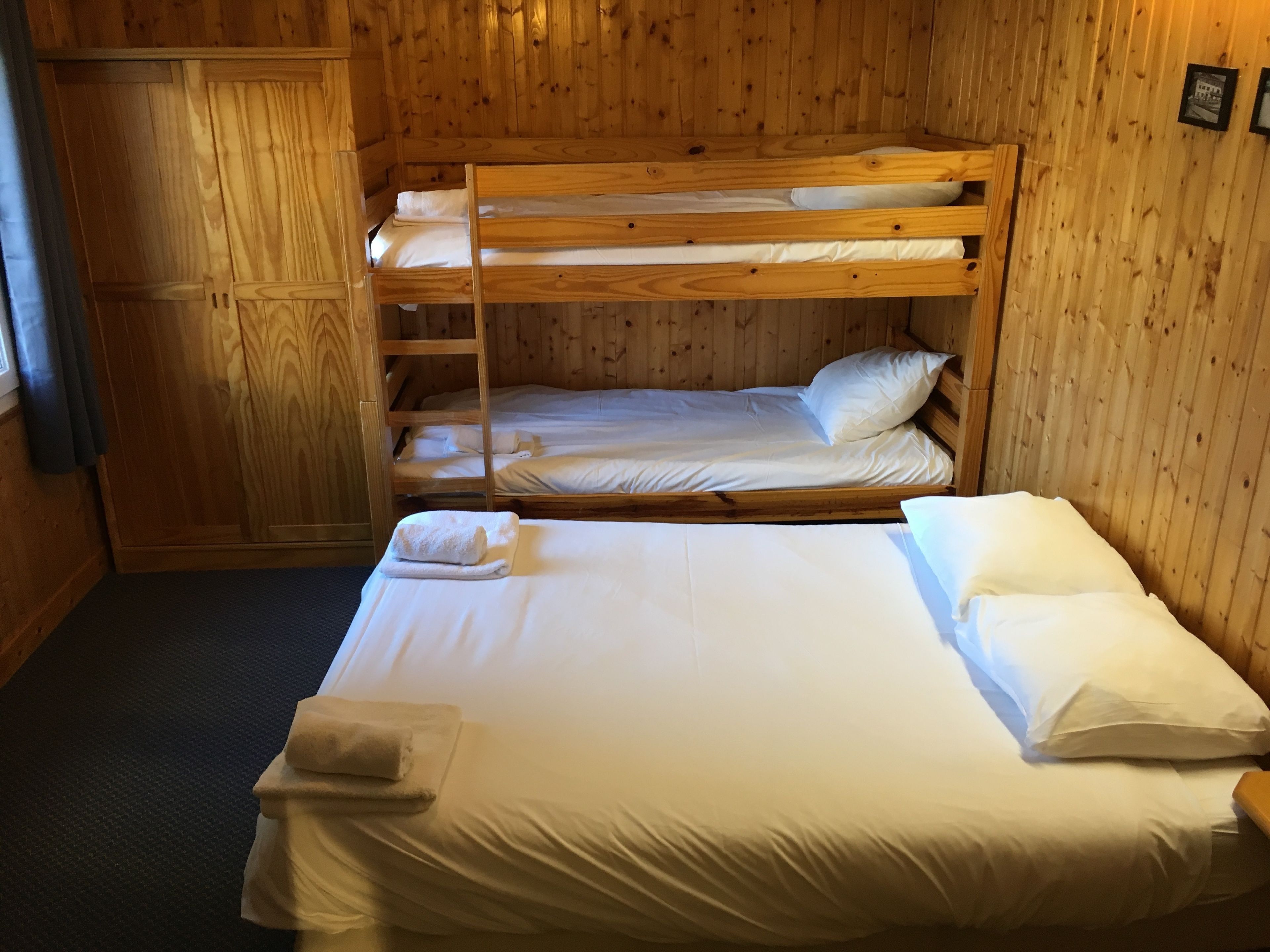 Habitación con literas, paredes de madera y una cama individual abajo.