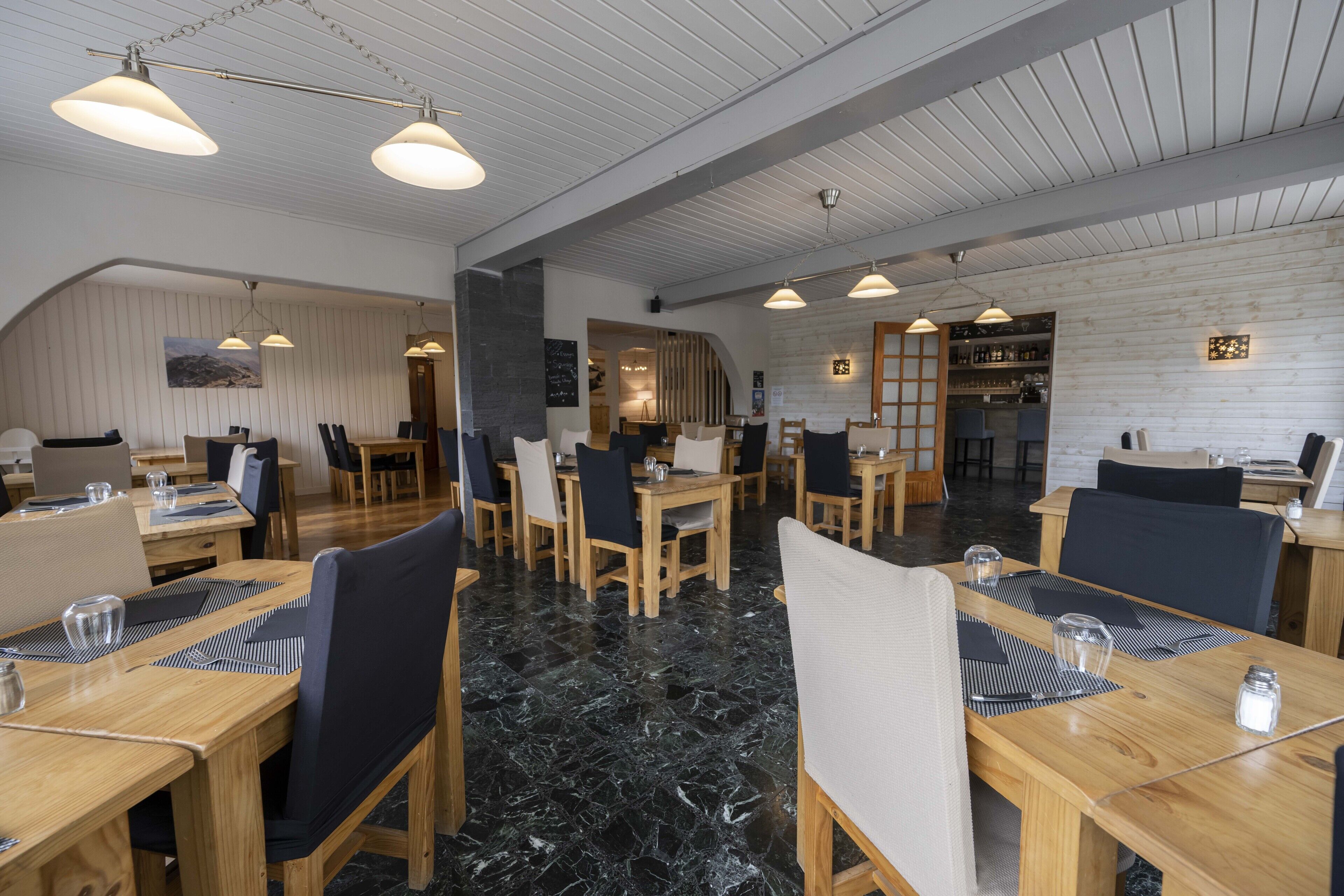 Un restaurante moderno con mesas y sillas de madera, suelo de mármol negro e iluminación colgante.