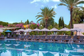 A pool with lounge chairs and umbrellas, surrounded by palm trees and flowers. - Miramare Beach Hotel (Manavgat)