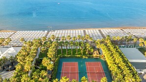 An aerial view of a resort with a tennis court, palm trees, and a beach. - Miramare Beach Hotel (Manavgat)