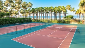 An outdoor tennis court with a net, surrounded by palm trees and a view of the ocean. - Miramare Beach Hotel (Manavgat)
