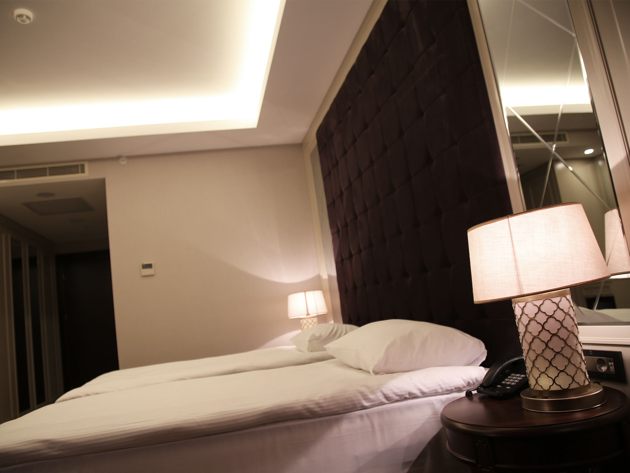 A hotel room with a bed, a bedside lamp, a telephone, and a mirror.