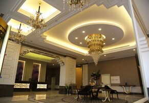 A lobby with a reception desk, seating area, chandeliers, and a staircase.