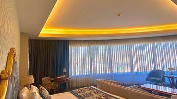 Et moderne hotelværelse med en stor seng, en sofa, et skrivebord og udsigt til det frie gennem lette gardiner.