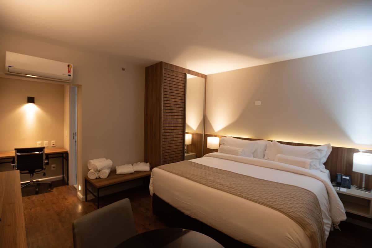 Una habitación de hotel con una cama grande, mesitas de noche con lámparas, un escritorio y una silla.