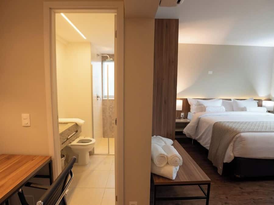 A hotel room with a bed, bedside table, and a view into the bathroom.