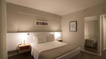 A hotel room with a large bed, bedside tables, a nightstand, a mirror, and a framed picture on the wall.