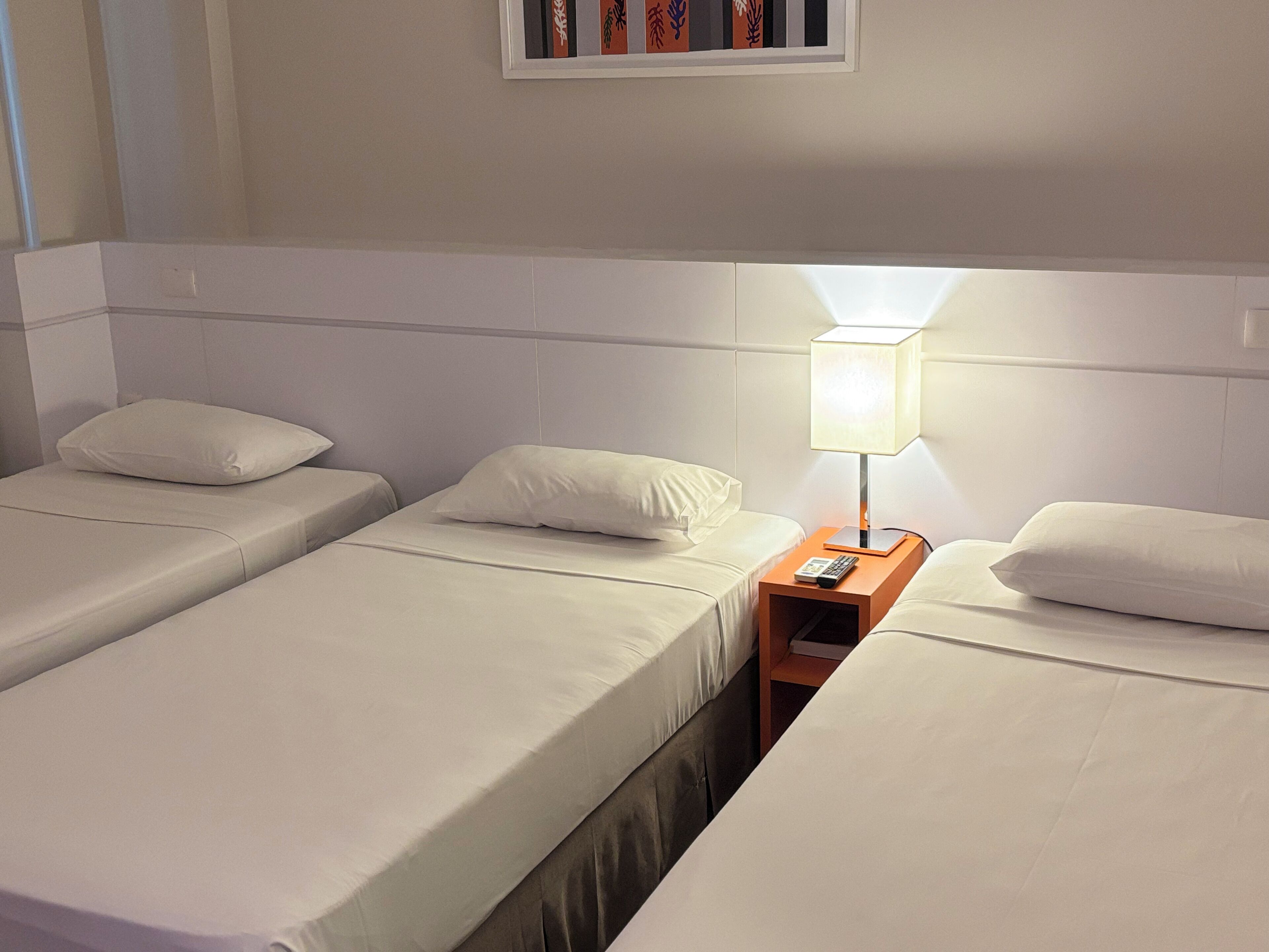 A hotel room with two single beds, a nightstand with a lamp, and a framed picture on the wall.