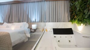 Habitación de hotel con dos camas, un ventanal con cortinas, una bañera y una planta en la pared.