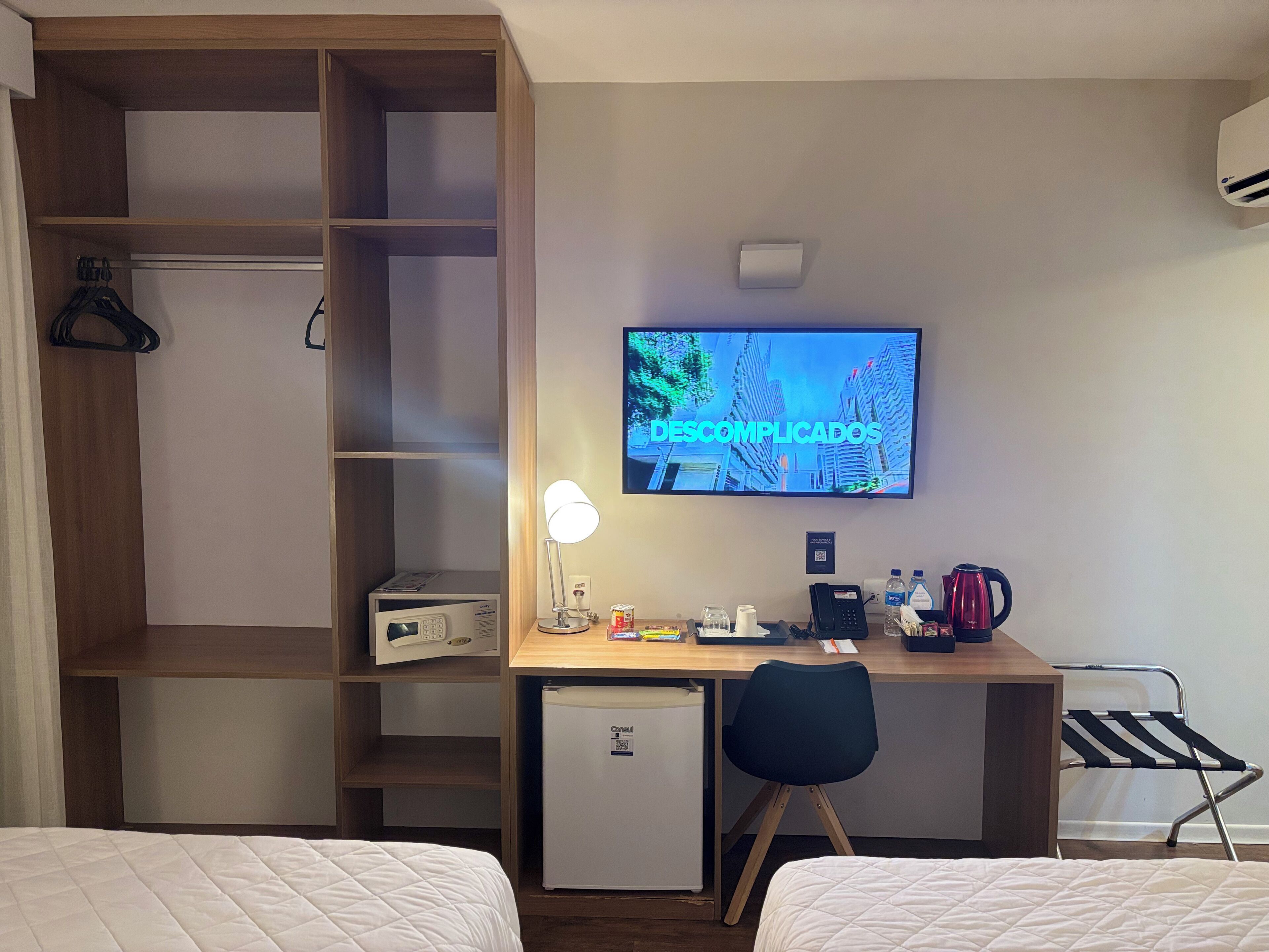 Habitación de hotel con escritorio, televisión, mini refrigerador, tetera y cama.